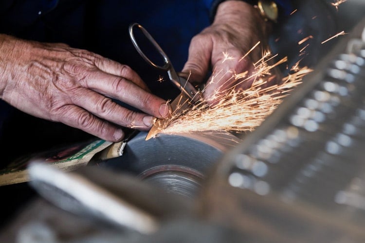 A craftsman grinding a scissor blade, sparks flying, in the Sheffield workshop